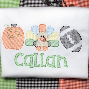 May include: A white t-shirt with an embroidered pumpkin, turkey, and football. The name "Callan" is embroidered in green below the images.
