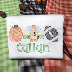 May include: White onesie with an embroidered pumpkin, turkey, and football. The name "Callan" is embroidered in green below the images.