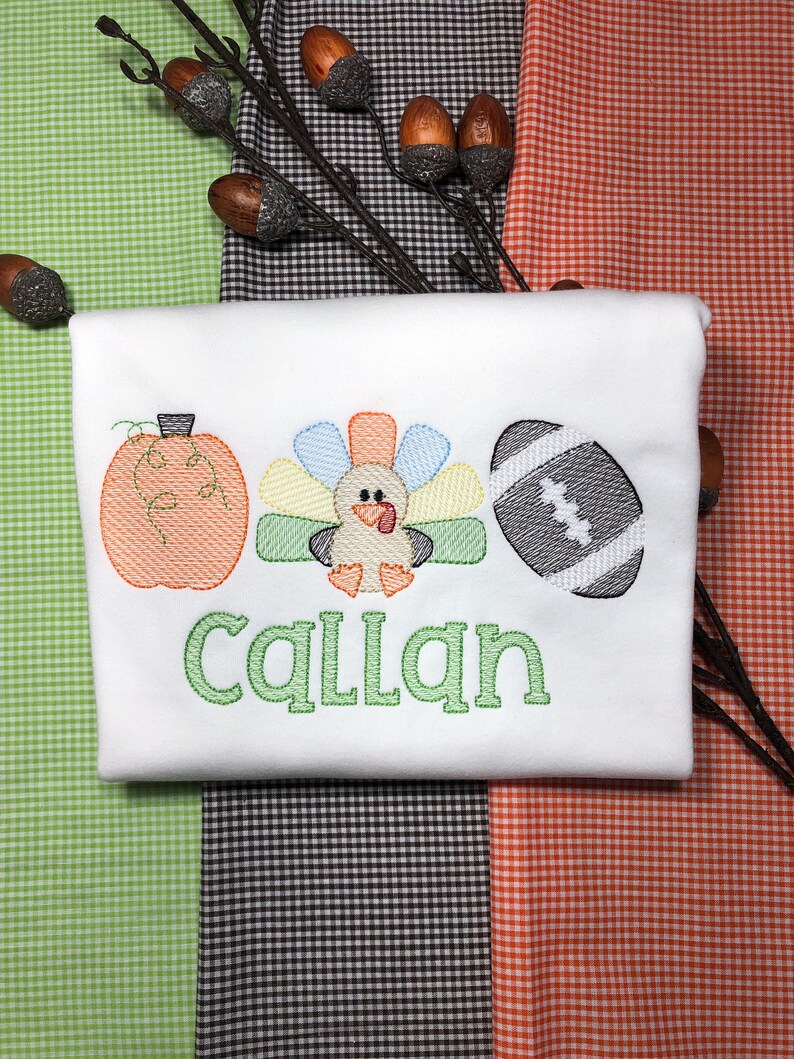 May include: White onesie with an embroidered pumpkin, turkey, and football. The name "Callan" is embroidered in green below the images.