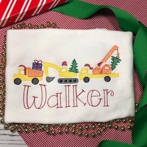May include: A white long-sleeve shirt with an embroidered design of construction vehicles hauling a Christmas tree. The name "Walker" is embroidered below the design.
