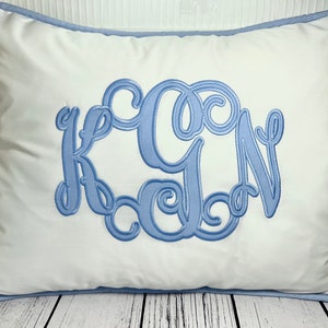 May include: White pillow with a blue embroidered monogram of the letters "KGN" in a decorative script font.