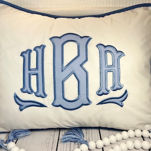 May include: White pillow with blue embroidered monogram "HBA" and blue tassels.