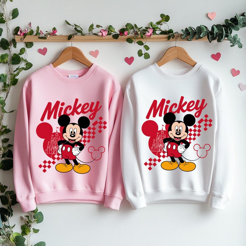 May include: Two sweatshirts, one pink and one white, each featuring a Mickey Mouse graphic. The design includes the word "Mickey" in red script, a cartoon image of Mickey Mouse, and a castle silhouette.