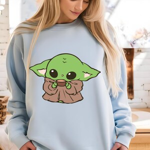Peut inclure: Sweat-shirt bleu clair avec une illustration de dessin animé d'un personnage extraterrestre vert tenant une tasse marron. L'extraterrestre a de grands yeux noirs et de grandes oreilles.