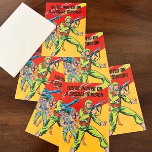 May include: A stack of invitation cards with a retro comic book style. The cards feature a soldier in green and red uniform, holding a weapon, with the text "YOU'RE INVITED ON A SPECIAL MISSION" on a yellow background.