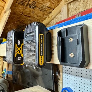 May include: A wall-mounted power tool battery holder with two black and yellow 20V DeWalt batteries and a black holder. The batteries are labeled "20V MAX Lithium Ion" and "XR 5 AH". The holder is mounted on a wooden surface.