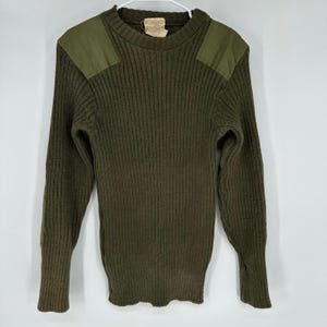 May include: An olive green ribbed knit sweater featuring a crew neckline and solid olive green fabric patches on both shoulders. The long-sleeved garment has a thick, textured vertical knit pattern and a tag visible at the inner collar area.