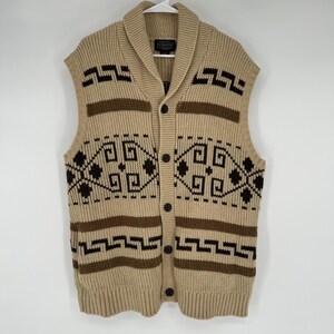 May include: A beige knit sweater vest featuring a shawl collar and a button-front closure. The garment displays dark brown geometric patterns and horizontal stripes across the chest and hem. A Pendleton brand label is visible at the neckline.