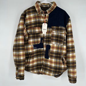 May include: A brown, yellow, and white plaid flannel shirt with navy blue patches and white stitching. The shirt has two chest pockets and a button-down front. The shirt is hanging on a white hanger.