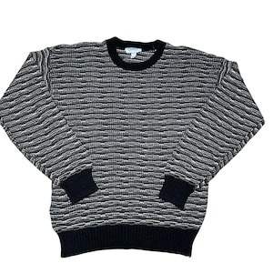 May include: A crew neck sweater with a textured pattern in black, white, and olive green. The cuffs, hem, and collar are solid black. The sweater is made of a knit fabric.