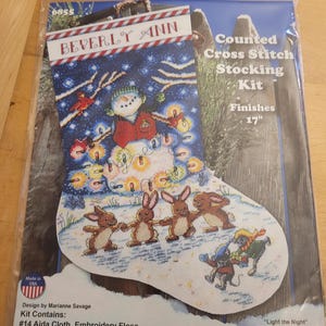 May include: A Beverly Ann counted cross stitch stocking kit titled Light the Night. The packaging shows a 17 inch stocking design featuring a snowman with colorful lights, four brown rabbits, and two mice in a snowy landscape with red birds.
