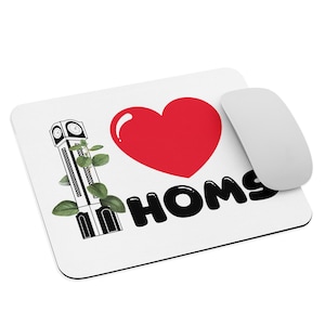 Puede incluir: Alfombrilla de ratón blanca con un corazón rojo, las palabras "I Homs" en negro y una ilustración en blanco y negro de una torre del reloj con hojas verdes. Un ratón de ordenador blanco está a la derecha.
