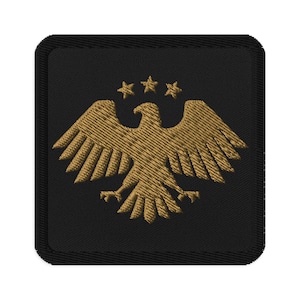 May include: Embroidered patch with a gold eagle and three stars on a black background. The patch is square with rounded corners and a black border. The eagle has outstretched wings.