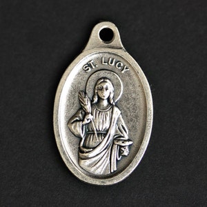 May include: Silver oval pendant with a depiction of Saint Lucy, a halo, and the text "ST. LUCY".