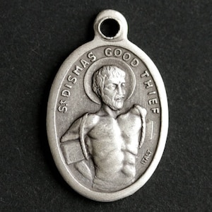 Może przedstawiać: Srebrny wisiorek z reliefowym wizerunkiem mężczyzny z aureolą, tekstem "St. Dismas Good Thief" i "Italy" na przodzie.