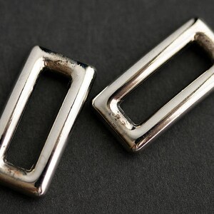 May include: Two silver metal rectangular rings with a smooth finish. The rings have a rectangular opening in the center.