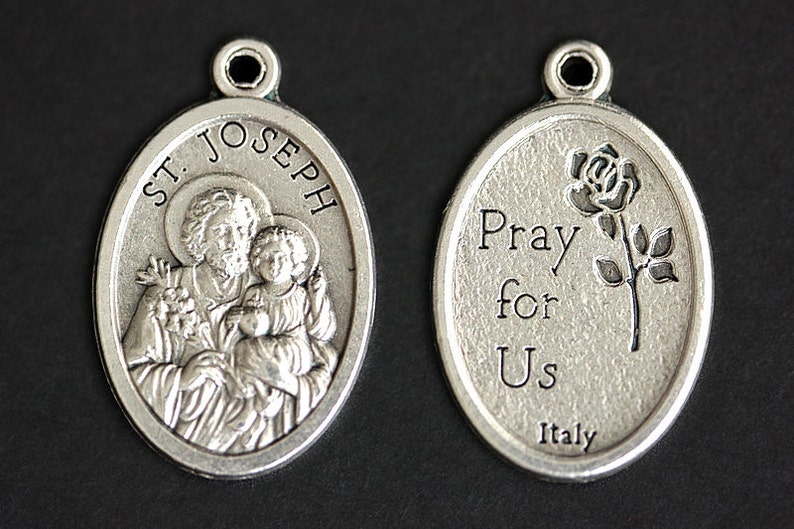 May include: Silver oval pendant with a depiction of Saint Joseph holding the baby Jesus on one side and the words "Pray for Us" and a rose on the other side. The pendant is made in Italy.