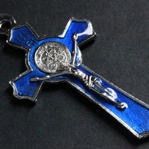 Puede incluir: Un colgante de cruz de metal plateado y azul con una representaci&oacute;n de Jesucristo en la cruz. La cruz tiene un acabado de esmalte azul y un bucle de metal plateado en la parte superior.