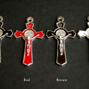 Puede incluir: Cuatro crucifijos de metal con una medalla de San Benito en el centro. Los crucifijos son negros, rojos, marrones y blancos.