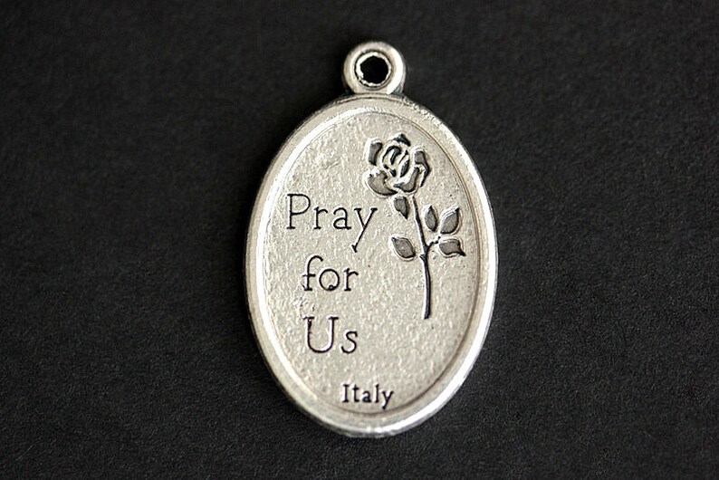 May include: Silver oval charm with a rose and the words "Pray for Us" and "Italy" engraved on it.