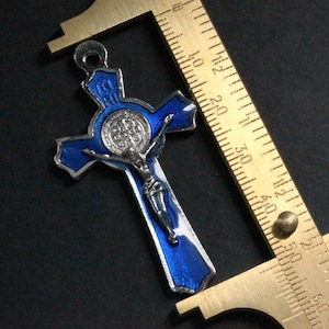 Puede incluir: Un colgante de esmalte azul de San Crist&oacute;bal con un crucifijo plateado y una medalla plateada con las palabras "IN RI" en la parte superior. El colgante se mide con una regla.