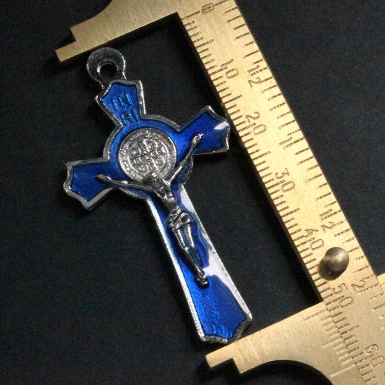 Puede incluir: Un colgante de esmalte azul de San Crist&oacute;bal con un crucifijo plateado y una medalla plateada con las palabras "IN RI" en la parte superior. El colgante se mide con una regla.