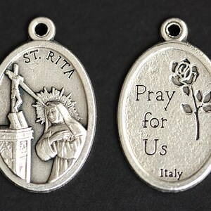 May include: Silver oval pendant with a depiction of Saint Rita of Cascia on one side and the words "Pray for Us Italy" and a rose on the other side.