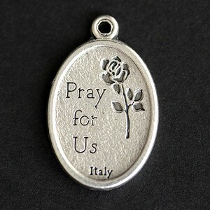 May include: Silver oval pendant with the words "Pray for Us" and a rose design. The pendant is made in Italy.
