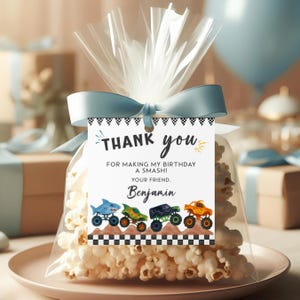 May include: A clear cellophane bag filled with popcorn, tied with a light blue ribbon. A tag reads "Thank you" and "For making my birthday a smash!" with a row of monster truck illustrations. The tag is personalized with the name "Benjamin".