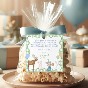 Könnte beinhalten: Ein klarer Zellophanbeutel gefüllt mit Popcorn, gebunden mit einem hellblauen Band. Ein grün-weißes Vichy-Etikett ist angebracht, mit Cartoon-Tieren und dem Text: "If you give a mouse a celebration... he'll be grateful for friends like you. Thanks for coming!"