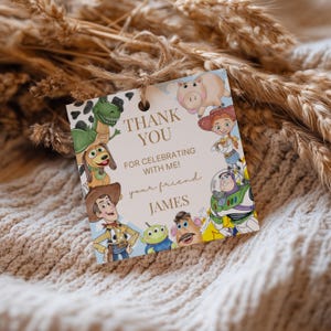 May include: A square gift tag with a light blue background and illustrations of characters from the Toy Story movie. The tag reads "THANK YOU FOR CELEBRATING WITH ME! your friend JAMES."
