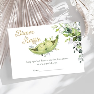 May include: A white baby shower raffle card with the words "Diaper Raffle" in gold script. The card features a watercolor illustration of two smiling peas in a pod and floral accents. The text reads, "Bring a pack of diapers, any size, for a chance to win a special prize."