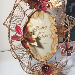 May include: Ornate gold-colored metal picture frame with an oval opening. The frame features decorative red and gold floral accents and a mesh ribbon design. The text "Pretty as a Picture" is visible on the frame's insert, which measures 6" x 6" (10.1cm x 15.2cm).