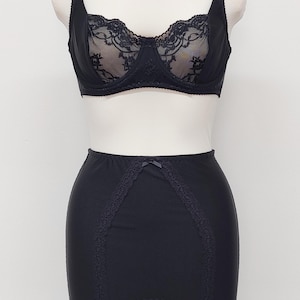 May include: A black lingerie set comprising a bra with lace detailing and a high-waisted girdle. The bra has adjustable straps and underwire support. The girdle features lace trim and garter straps.