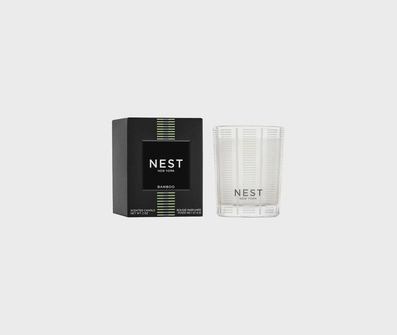 May include: A black and green scented candle with the text "NEST NEW YORK" and "BAMBOO" on the label. The candle is in a clear glass jar with a black lid.