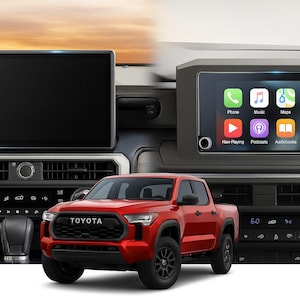 May include: A red Toyota pickup truck is parked in front of a dashboard with two infotainment screens. One screen displays a blank interface, while the other shows an Apple CarPlay interface with app icons. The dashboard has air vents and climate controls.