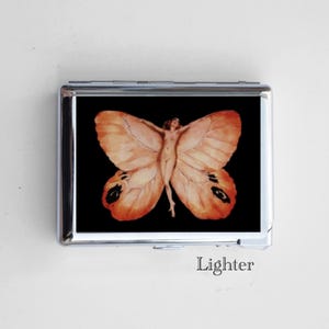 May include: A silver metal lighter featuring a butterfly design. The artwork depicts a nude figure with outstretched arms, integrated into the butterfly's wings. The wings are a blend of orange and brown hues against a black background. The word "Lighter" is printed at the bottom.