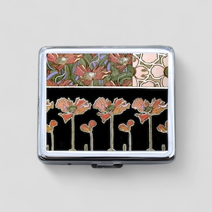 May include: A silver compact with a floral design featuring red poppies on a black background. The top of the compact has a patchwork design of red poppies on a green and purple background and white flowers on a pink background.