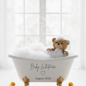 May include: A white claw-foot bathtub filled with bubbles, featuring a teddy bear. The tub has gold-colored feet and the text "Baby Whitmore" with a heart and "August 2026". Two yellow rubber duckies sit nearby. Bubbles float in the background.