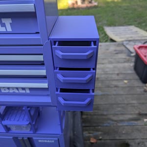 May include: A purple metal tool chest attachment featuring three small, stacked drawers with matching purple handles. The unit is mounted to the side of a larger purple Kobalt tool cabinet, which has silver drawer pulls and visible branding.