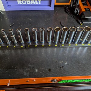 May include: A set of seventeen silver-colored metal socket tools arranged in ascending order on a black plastic rail. Each socket is labeled with a number from 6 to 22, printed in yellow on the base, with blue rings at the base of each tool.
