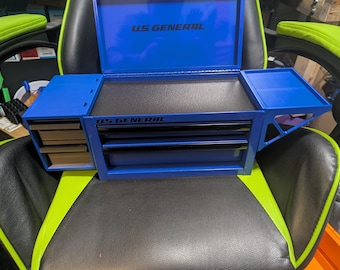 May include: A blue US GENERAL toolbox with multiple drawers and compartments. The toolbox is open, revealing a black interior and the US GENERAL logo. It is sitting on a black and green chair.