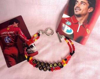 May include: A beaded bracelet with black, red, and yellow beads. The bracelet spells out "Leclerc 16" in black letters.