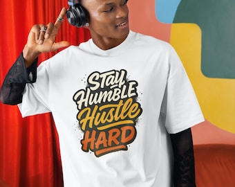 May include: White t-shirt with the text "Stay Humble Hustle Hard" in a stylized design. The shirt has a crew neck and short sleeves. The person in the image is wearing black headphones and black mesh sleeves.