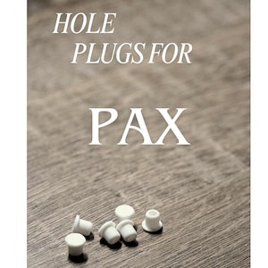 May include: White hole plugs for PAX are displayed on a wooden surface. The text "HOLE PLUGS FOR PAX" is printed in white. The plugs are small, cylindrical, and have a flat top.