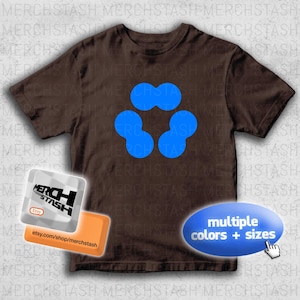 May include: A brown t-shirt featuring a blue abstract design. The shirt has a crew neck and short sleeves. The image also includes a shop logo and a callout that says "multiple colors + sizes".