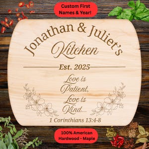 May include: A light-coloured, wooden chopping board with rounded edges. The board is engraved with the names "Jonathan & Juliet's Kitchen" and the year "Est. 2025." It also features the quote "Love is Patient, Love is Kind..." and floral designs. The text "100% American Hardwood - Maple" is also present.