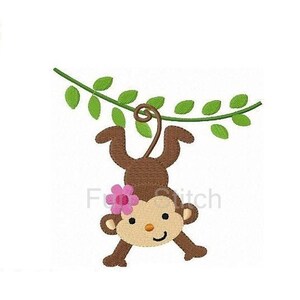 May include: A brown monkey with a pink flower on its head is hanging upside down from a green vine. The monkey is smiling and has its arms outstretched.