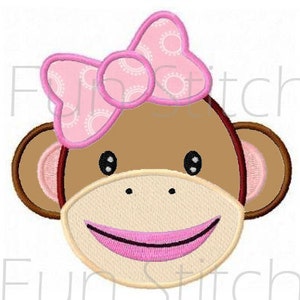 May include: A brown monkey face with a pink bow and a pink smile. The bow has a white polka dot pattern.