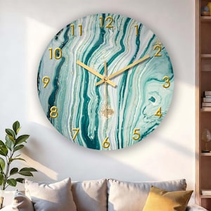 May include: Round wall clock with a teal and white marble design. The clock face features gold-colored numerals and hands. A decorative gold-colored pendulum hangs below the clock face. The clock is mounted on a white wall.